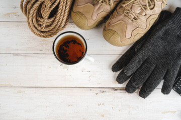 Fototapeta na wymiar Hiking boots with equipment for hiking, cup of tea on wooden board
