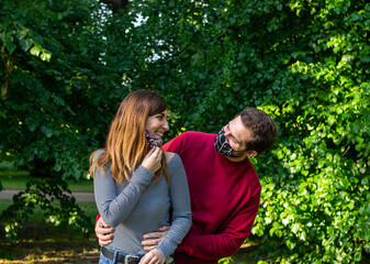 Photo of a young and attractive couple on a date in the park wearing a face mask and hugging