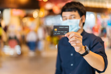 credit card with young asian man wearing medical mask at shopping mall for prevention from coronavirus (Covid-19) pandemic. new normal concepts