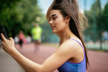 Young sporty woman resting on running track. Beautiful woman in sportswear using the phone