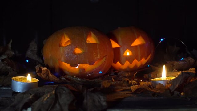 Halloween, two pumpkins with a scary glowing face inside, smoke passes from left to right in the dark at night. Candles are burning.