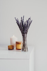 Dried lavender in a small glass vase and aroma candles on white table. Simple Living room decor....