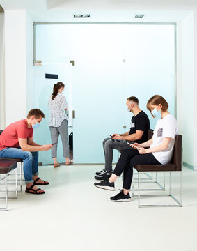 Young people in medical masks, sitting in a queue and waiting for a doctor's appointment in the hospital.