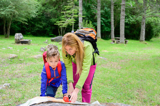 Mother Teaches Her Son How To Use The Compass On The Map, In A Forest.