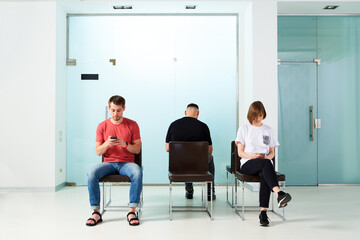 Young people sit in line to see a doctor at a clinic reading the news on their smartphones.