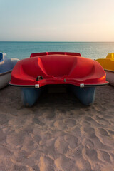 Pedal boats on the sunset on a tropical island beach. Red catamaran on an empty sea shore on evening landscape with sun rays. Wallpaper for desktop, poster, marine travel photo, post card design.