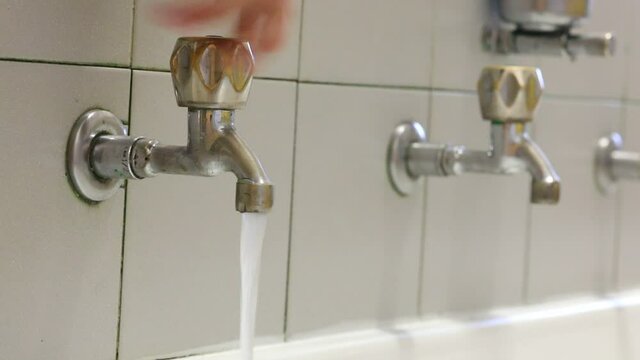 Hand of man closing a tap to block the flow of drinking water
