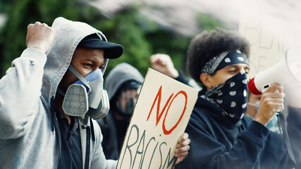 Mixed-races males protesters in respirators and masks protesting with colorful smoke and posters...