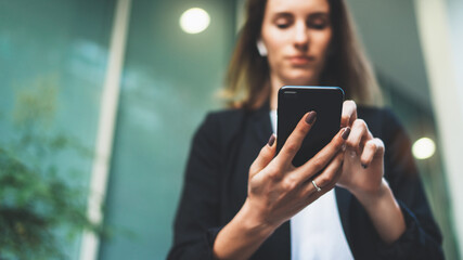 front view of a businesswoman holding a smartphone while sending messages. Confident female employee using a mobile app for online banking on a mobile device, standing next to office