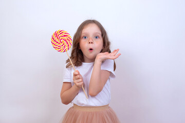 Happy little girl holds candy lollipop on a white background and is surprised
