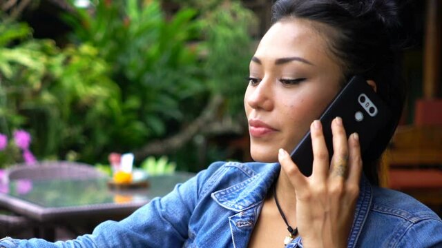 Young happy asian woman talking on cellphone and drinking water in cafe