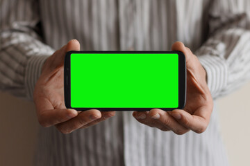 Smartphone with a green screen in hands, horizontal position, against the background of a man in a shirt.