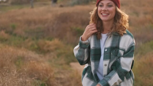 Happy blonde woman wearing hat and plaid shirt having fun and looking around while walking outdoors