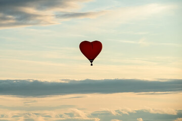 Colorful big hot air heart shaped balloon flying against the cloudy sky