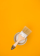 Paintbrush with a wooden handle on a metal can with paint on a yellow background, sitting on top. Copy space.