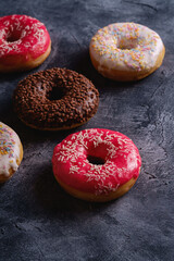 Chocolate, pink and vanilla donuts with sprinkles, sweet glazed dessert food on dark concrete textured background, angle view