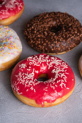 Chocolate, pink and vanilla donuts with sprinkles, sweet glazed dessert food on concrete textured background, angle view macro