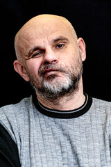 portrait of a middle-aged bald bearded man on a black background with the silly grin on his face