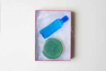 Box with filling material and cosmetic bottle and jar with lotion inside on yellow colored paper background