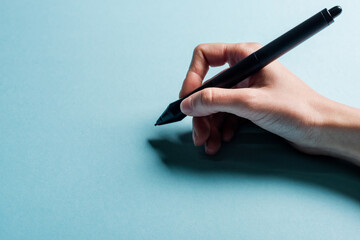 Cropped view of designer holding stylus of graphics tablet on blue background