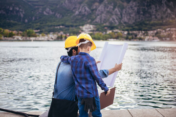 Harbor engineer with his son holding the paper, construction work, smiling.