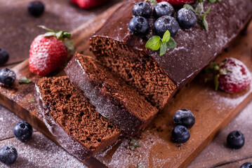 Fresh tasty homemade chocolate cake with icing with summer berries on a wooden table.