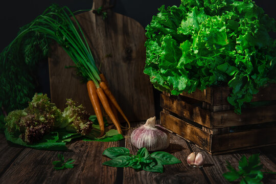 Rustic composition of vegetables and herbs: garlic, carrots, lettuce, spinach, on a wooden table and in a wooden box. Image with selective focus
