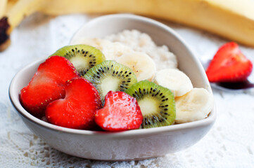 Breakfast with oatmeal with strawberries, kiwi, banana on white background. Breakfast for child. Oatmeal in a white heart-shaped plate