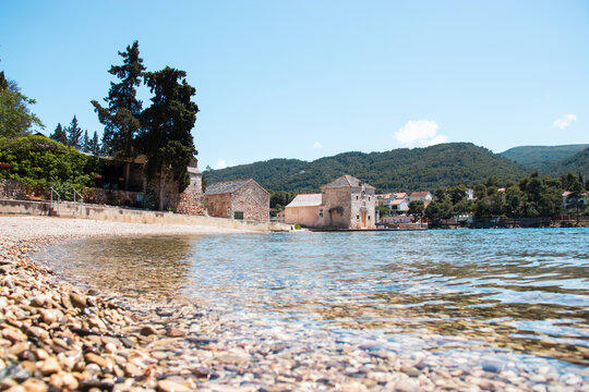 Small picturesque house of Saint Jerolim, stone greek style building standing on the waterfront of Starigrad,Hvar. Wide empty pebble beach stretching with clear sea on a warm summer day