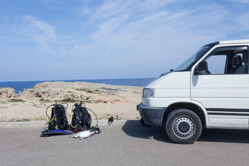 Fototapeta na wymiar Wanderlust concept of a summer image, traveling with a van and preparing to go has scuba diving on Majorca island. Diving equipment prepared on the ground and camper van 
