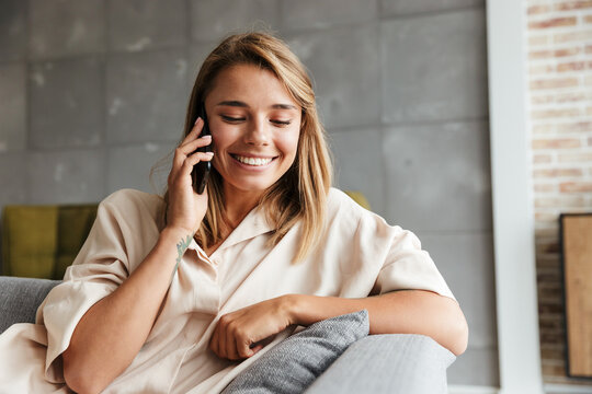 Image of woman smiling and talking on cellphone while sitting on couch