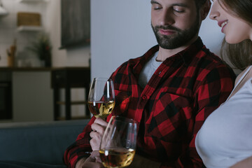 cropped view of smiling girl and handsome boyfriend sitting on sofa with glasses of white wine