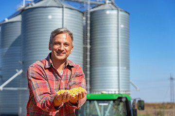 Smiling Farmer Showing Freshly Harvested Corn Grains Against Grain Silo