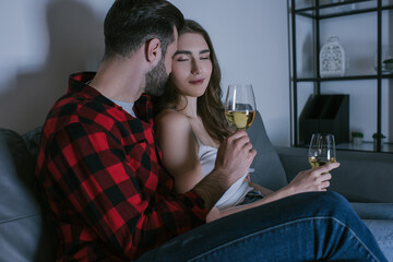 happy girl with closed eyes sitting on sofa near boyfriend with glasses of white wine