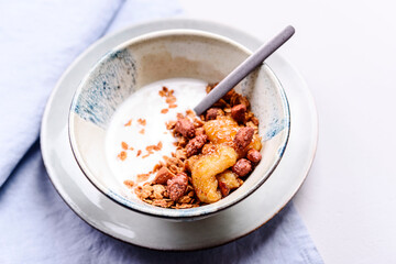 Healthy breakfast yogurt bowl with granola and caramelized bananas and nuts on grey concrete background. Selective focus