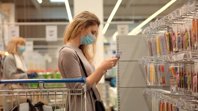 Woman Shopper Choosing Product In Hypermarket Store.Girl In Face Mask Shopping In Market On Covid19 Coronavirus Pandemic Quarantine Lock down. Bayer In Medical Mask In Supermarket Avoid Self Distance