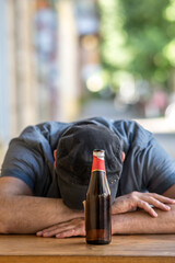 Pensive and sad man with bowed head sitting holding a bottle of beer outside a bar. Selective focus