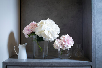 Pink and white hydrangeas in a glass vase and a white porcelain jug