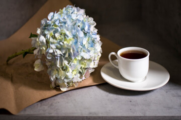 A branch of green pastel hydrangeain with white cup of coffee on a on a gray craft vintage background.