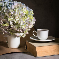A branch of green pastel hydrangeain an enameled mug instead of a vase on a on a gray craft vintage background. Copy space