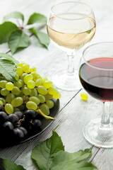 Two glasses with different varieties of wine and a plate with different ripe grapes. The concept of wine tasting