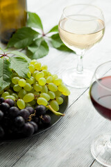 Two glasses with different varieties of wine and a plate with ripe grapes. Duet from a composition of red and white wine