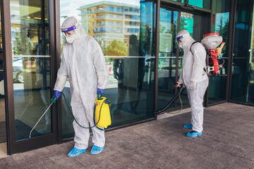 Professional workers in hazmat suits disinfecting outdoor of mall, pandemic health risk, coronavirus