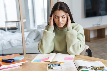 Photo of woman with headache rubbing her temples while doing homework