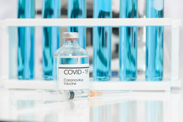 Bottle of coronavirus vaccine and syringe on white table.