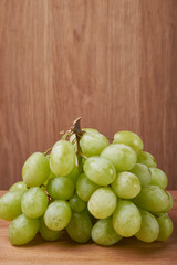 A bouquet of green grapes in a basket, autumn fruits, a symbol of abundance on a rustic background of a tree with a copy space, close-up.