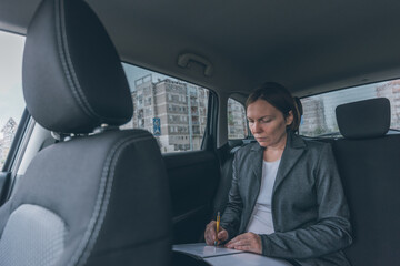 Businesswoman doing business paperwork on car back seat