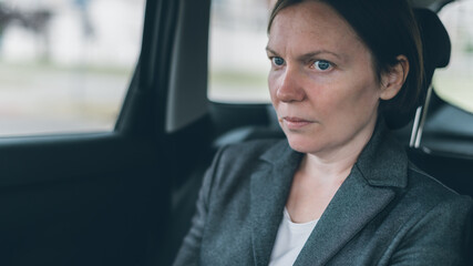 Worried businesswoman sitting at car back seat - obrazy, fototapety, plakaty