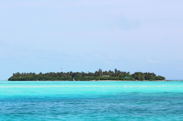 Small uninhabited Maldives island with green palm trees in azure waters of Indian ocean. Tropical beach vacation in luxury exotic resort