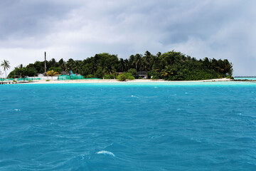 Small traditional village on Maldives island, green palm trees in azure waters of Indian ocean. Tropical beach vacation in luxury exotic resort